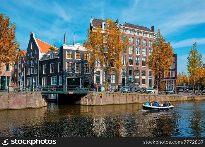 Amsterdam view - canal with tourist boat, bridge and old houses. Amsterdam, Netherlands. Amsterdam view - canal with boat, bridge and old houses