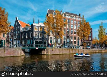 Amsterdam view - canal with tourist boat, bridge and old houses. Amsterdam, Netherlands. Amsterdam view - canal with boat, bridge and old houses