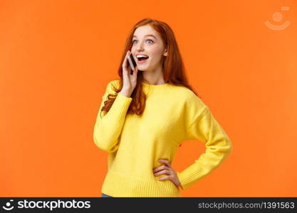 Amused and surprised smiling redhead girl widen eyes and look impressed as hear good news from friend during talking on phone, holding smartphone near ear, have conversation, orange background.. Amused and surprised smiling redhead girl widen eyes and look impressed as hear good news from friend during talking on phone, holding smartphone near ear, have conversation, orange background