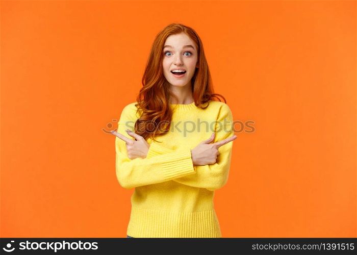 Amused dreamy and cute redhead girl asking advice in shopping mall, buying holiday presents, want valentines day gift, pointing sideways left and right, smiling upbeat, orange background.. Amused dreamy and cute redhead girl asking advice in shopping mall, buying holiday presents, want valentines day gift, pointing sideways left and right, smiling upbeat, orange background