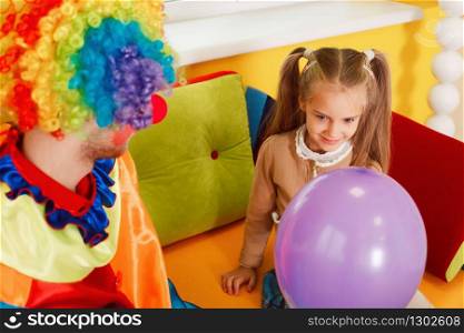 Amusing clown give air balloon to the little girl. Clown in colorful costume on birthday party.. Amusing clown give air balloon to the little girl