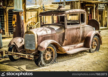 An abandoned car sits rusting away next to a fuel pump in the desert.