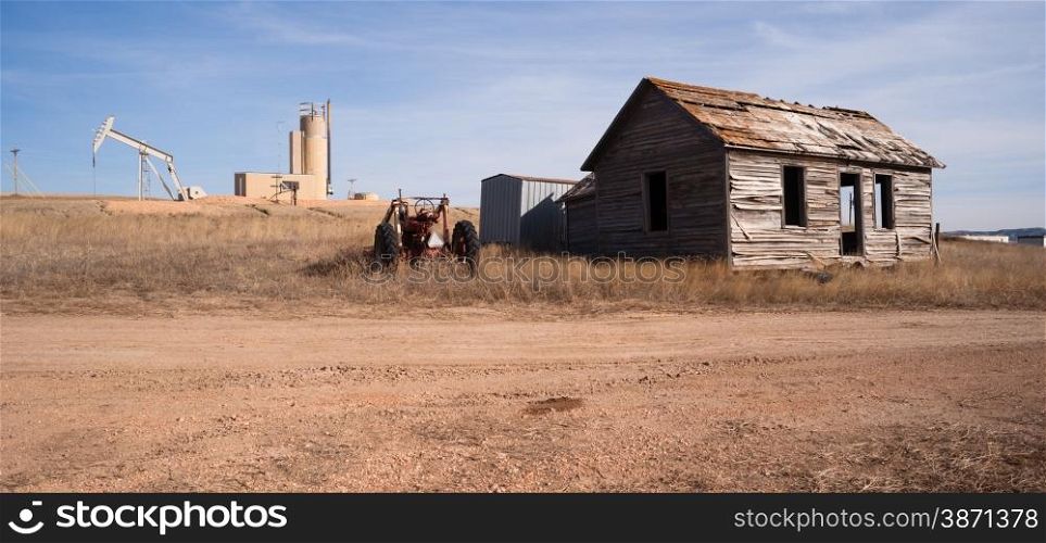 An abandoned tractor and cabin sit in the foreground of a fracking oil pump jack