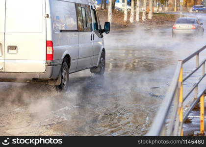 An accident on a heating main, a breakthrough in a pipe with hot water, cars drive along a flooded road, water vapor forms a smokescreen over the asphalt, image with copy space.. The road flooded with hot water after the breakthrough of the city heating main.