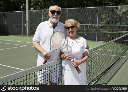 An active senior couple in sunglasses getting ready to play tennis.