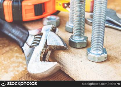 An adjustable spanner lies near the bolts and nuts of the washer against the background of wooden boards. The concept of tools and repair work.. An adjustable spanner lies near the bolts and nuts of the washer against the background of wooden boards.