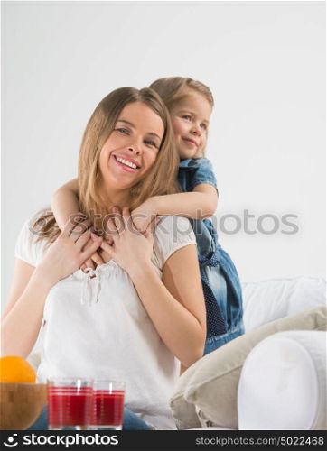 An adorable young girl hugging her mother's neck from behind
