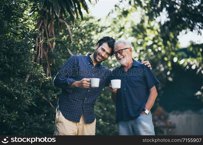 An adult hipster son and his senior father in garden, hugging
