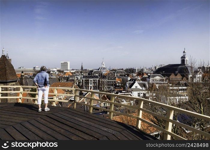 an adult woman stands with her hands in her back pockets, looking at the circuit of a windmill in schiedam, at the skyline with the houses and churches. woman looking at the skyline of schiedam