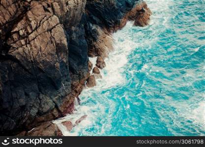 An aerial shot of the crystal water sea touching the rocks of the bottom of a mountain
