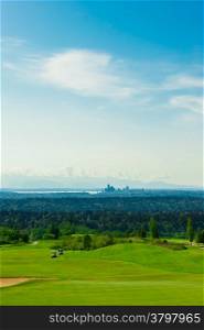 An aerial view from the top of the hill in a green golf course with Seattle downtown at the background.