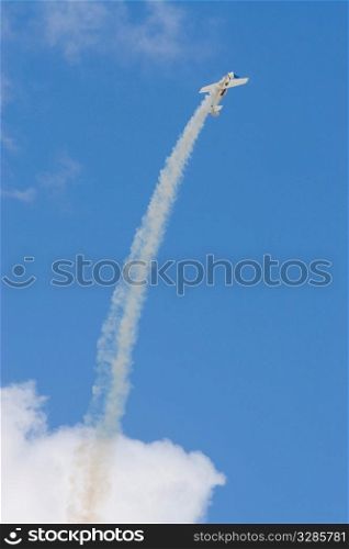 An aerobatic airplane trailing smoke flies up in smooth arc into a bright blue sky