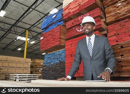 An African American male contractor standing in front of stacked wooden planks