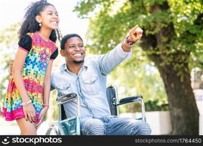 An african american man in a wheelchair enjoying a walk outdoors with his daughter.