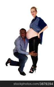 An African American man kneeling before his Caucasian wife, listenson her baby belly, isolated for white background.