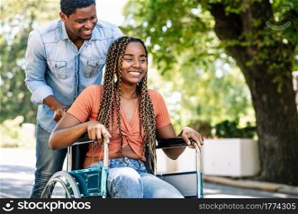 An african american woman in a wheelchair enjoying a walk with her boyfriend outdoors on the street.. Woman in a wheelchair enjoying a walk with her boyfriend.
