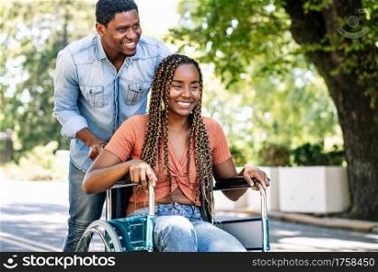 An african american woman in a wheelchair enjoying a walk with her boyfriend.