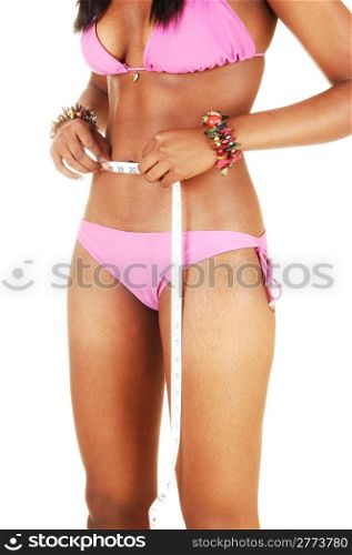 An African American young woman with a perfect body measuring hersmall waistline, in a pink bikini for white background.