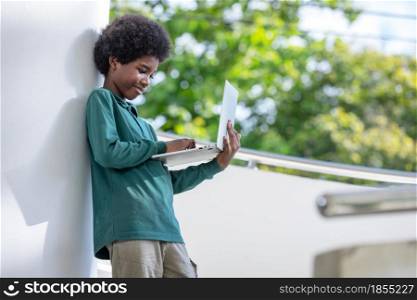 An African curly haired boy playing on his laptop in the afternoon stairway downstairs.