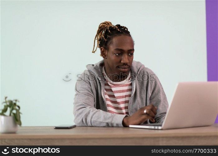 an afro young man sits in his home office during a pandemic and uses laptop for online meeting  
