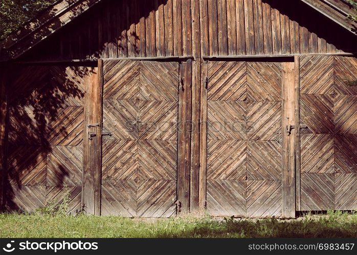 An aged, rural farm building with two doors and rusted locks with a rustic natural wooden facade and decorative woodwork in a creative pattern made out of weathered wood planks.. An aged, rural farm building with two doors and rusted locks with a rustic natural wooden facade and decorative woodwork in a creative pattern made out of weathered wood planks