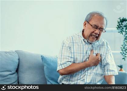 An agonizing senior man suffering from chest pain or heart attack alone in his living room. Serious health problem and feeling unwell concept for seniors.. An agonizing senior man suffering from chest pain or heart attack.