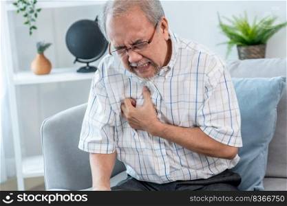 An agonizing senior man suffering from chest pain or heart attack alone in his living room. Serious health problem and feeling unwell concept for seniors.. An agonizing senior man suffering from chest pain or heart attack.