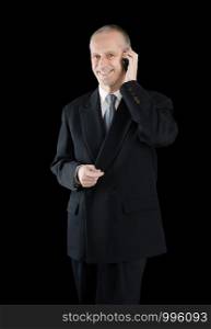 An agreeable businessman wearing a black suit smiling while speaking on mobile phone, on black background