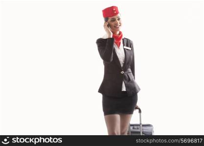 An air stewardess using cell phone while pulling luggage bag isolated over white background