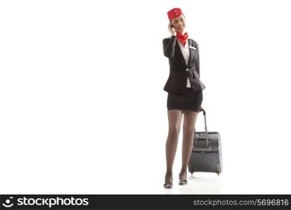 An airhostess using cell phone while pulling luggage bag isolated over white background