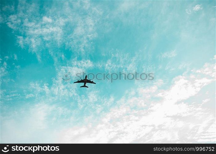 An airplane in flight against light blue sky and clouds. Abstract pastel beautiful landscape at sunset.
