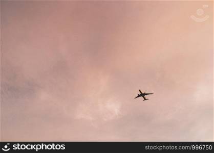 An airplane in flight against rainbow colorful sky and clouds. Abstract pastel beautiful landscape at sunset.