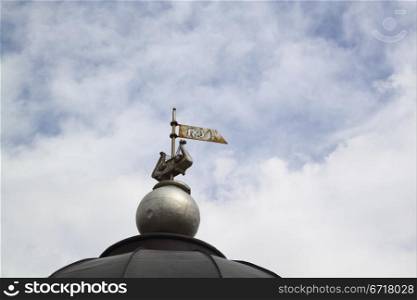 An ancient weather vane against the sky and clouds