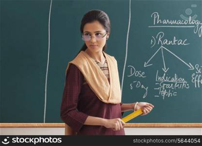 An angry female lecturer holding ruler against green board