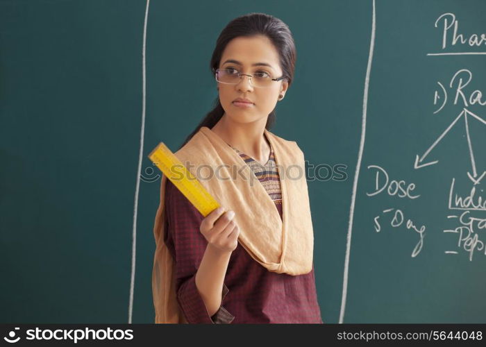 An angry young female teacher holding ruler against chalkboard