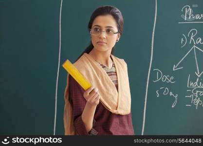 An angry young female teacher holding ruler against chalkboard