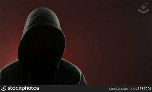 An anonymous, threatening thug wearing a hood stares at the camera in front of a red background. Centered version also available.