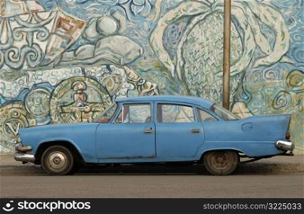 An antique car parked at the side of a graffiti covered wall, Havana, Cuba