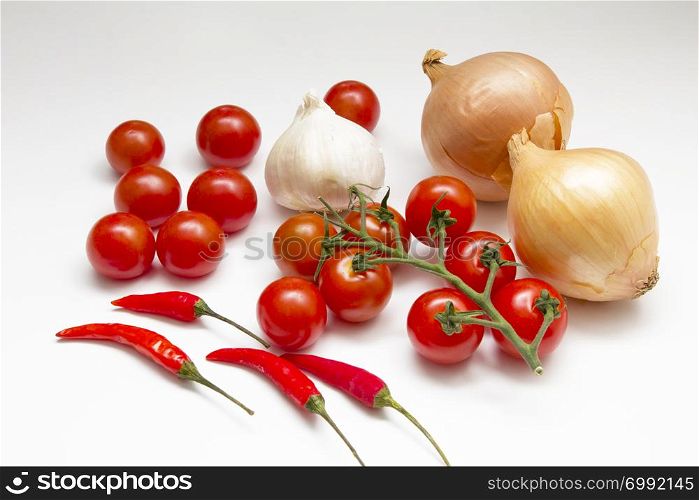 An arrangement of onons, tomatoes, chillies and garlic on a white background