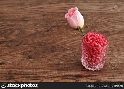 An artificial rose in a glass filled with pink beads