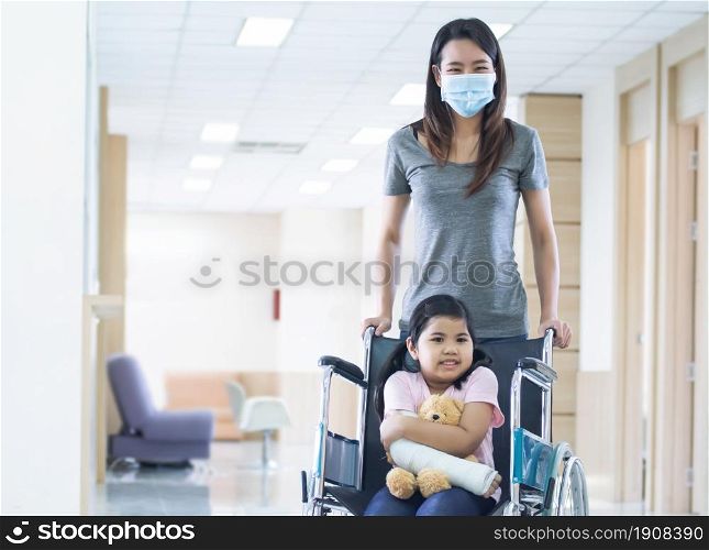 An asian beautiful woman is smiling and taking care her daughter while the little girl is getting accident and staying on wheelchair in hospital. Medical and Insurance Concept.