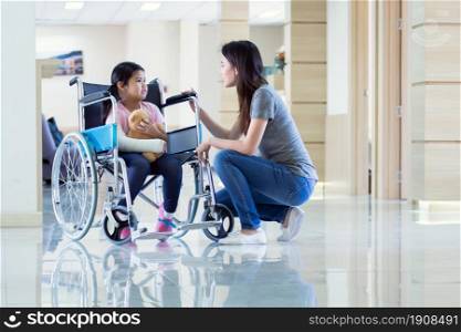 An asian beautiful woman is smiling and taking care her daughter while the little girl is getting accident and staying on wheelchair in hospital. Medical and Insurance Concept.