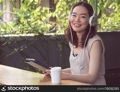 An asian beautiful woman is using headphone and tablet for listening to music with happy at home.