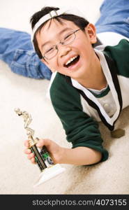 An asian boy excited aboyt his winning sport medal and trophy