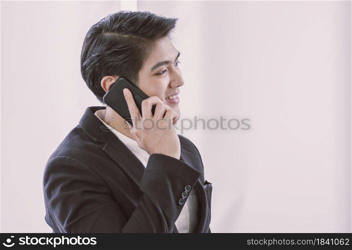 An Asian business man in formal suit is talking via mobile phone