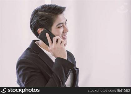 An Asian business man in formal suit is talking via mobile phone