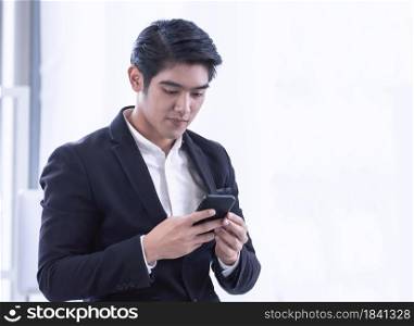 An Asian business man is smiling while texting message via mobile phone