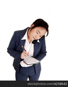 An Asian business woman talking on the phone a making notes in herin her day timer, on white background.