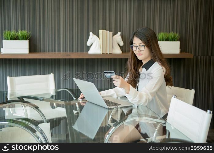 An Asian business woman using a credit card in front of a laptop