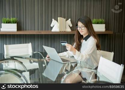 An Asian business woman using a credit card in front of a laptop